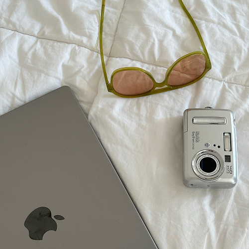 Laptop flatlay on bed with sunglasses and digital camera - Planoly